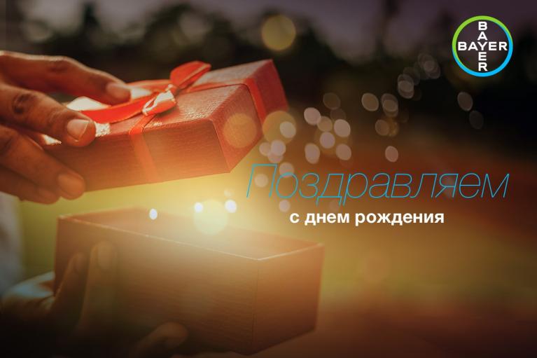 A person opens a red gift box with a ribbon. Russian text reads "Поздравляем с днем рождения," meaning "Happy Birthday." The Bayer logo is in the top right corner.