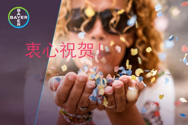 Person blowing colorful confetti, Bayer logo in the corner, and red Chinese text overlaid on the image.