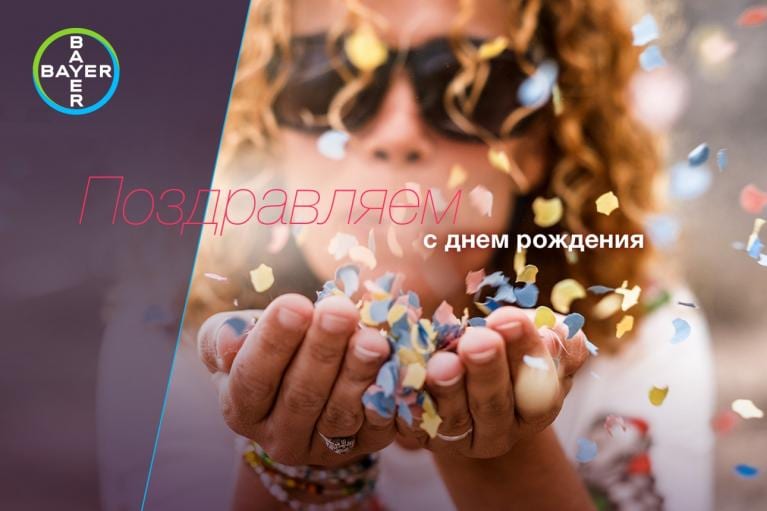 Person blowing colorful confetti from hands, wearing sunglasses. Text in Russian reads "Поздравляем с днем рождения" with Bayer logo in the corner.