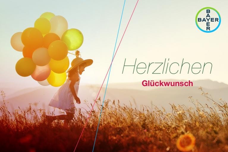 Girl running with balloons in a field at sunset. The words "Herzlichen Glückwunsch" and the Bayer logo are visible.
