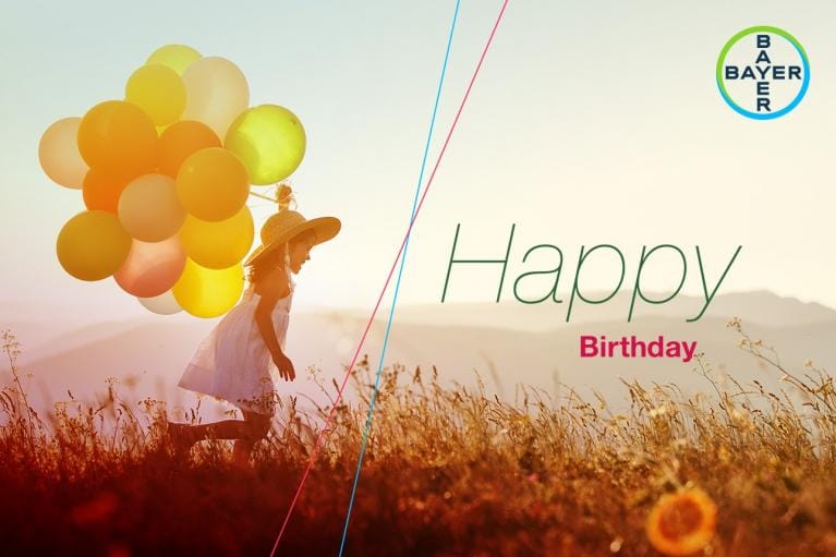 A child running with colorful balloons in a sunlit field, wearing a hat. "Happy Birthday" text and a Bayer logo are on the right.