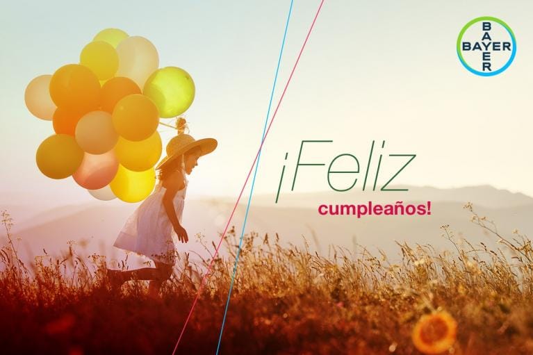 A child in a field holds colorful balloons under a sunset sky, with the text "¡Feliz cumpleaños!" and the Bayer logo in the top right corner.