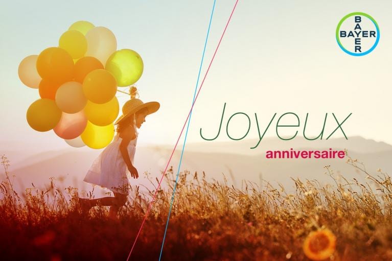 Child with balloons in a field, wearing a straw hat. Text reads "Joyeux anniversaire" with Bayer logo in the corner.