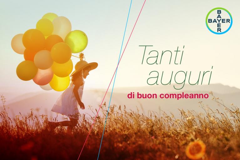 Child with balloons running through a field under a sunny sky. Text reads "Tanti auguri di buon compleanno" with Bayer logo.