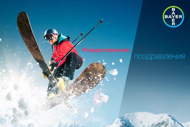A skier in mid-air performs a jump, surrounded by snow. The Bayer logo and Russian text are present in the background.