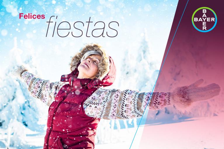Person in a winter coat enjoying the snow, with arms outstretched, under the text "Felices fiestas." Bayer logo in the corner.