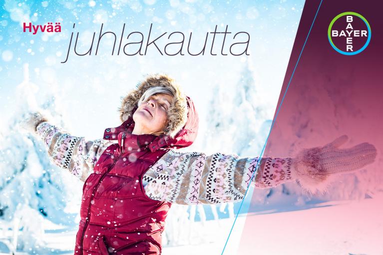 Person in a red jacket and knitted gloves joyfully stands in a snowy landscape with arms outstretched. Finnish text and Bayer logo are present.