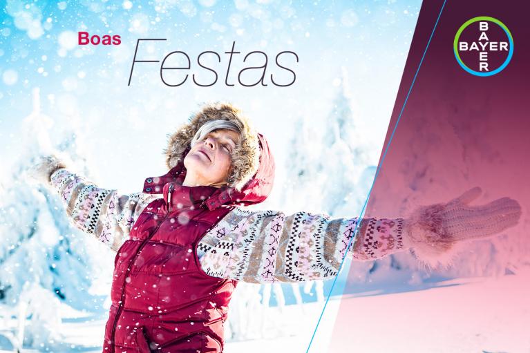 Person in winter clothing joyfully spreads arms in a snowy landscape. Text reads "Boas Festas" with a Bayer logo in the corner.