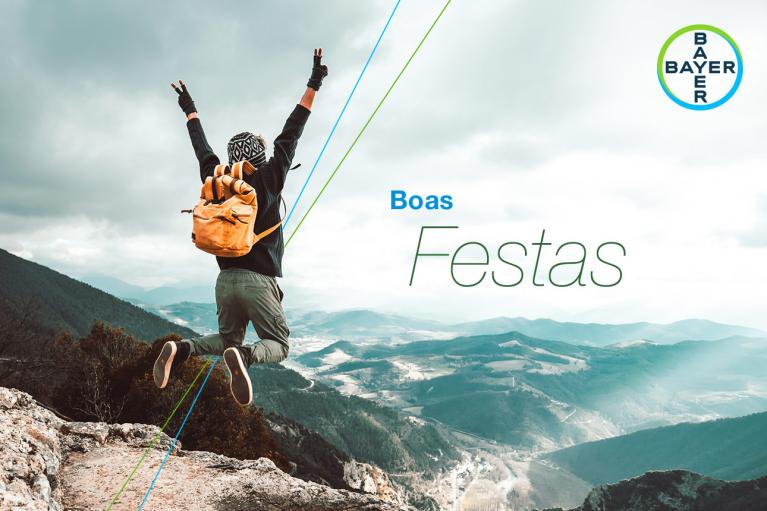 Person with an orange backpack jumps on a mountain cliff, overlooking a vast landscape. "Boas Festas" and Bayer logo are in the sky.