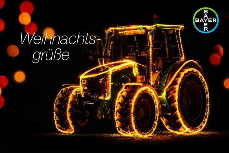 A tractor is decorated with Christmas lights against a dark background. The text "Weihnachtsgrüße" is on the left, and the Bayer logo is on the right.