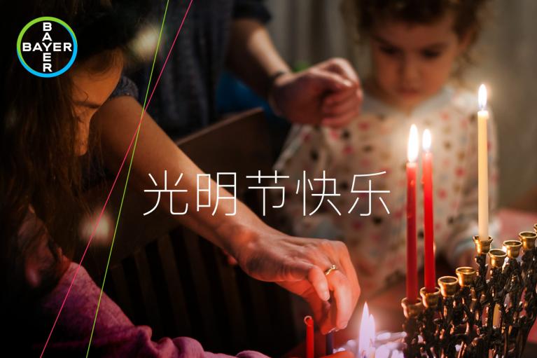Two people light candles on a menorah. The Bayer logo is in the corner, and Chinese text translates to "Happy Festival of Lights.