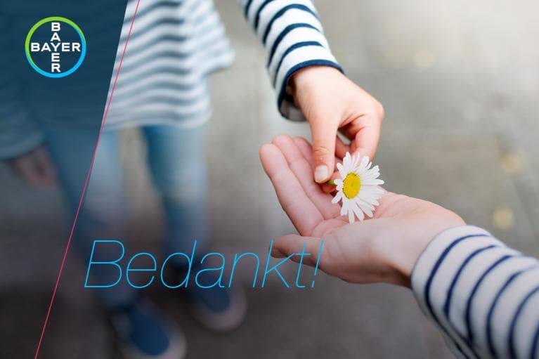 A person hands a daisy to another person wearing striped sleeves. The word "Bedankt!" and the Bayer logo are visible.