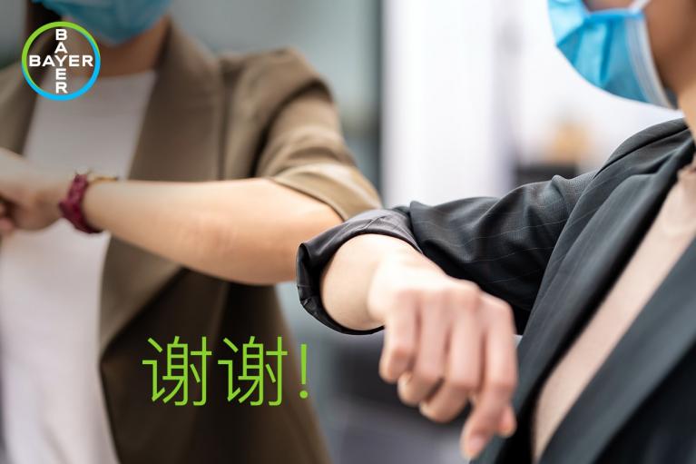 Two people wearing masks greet each other with an elbow bump. The Bayer logo is in the top left corner, and the word "谢谢" is displayed in green.