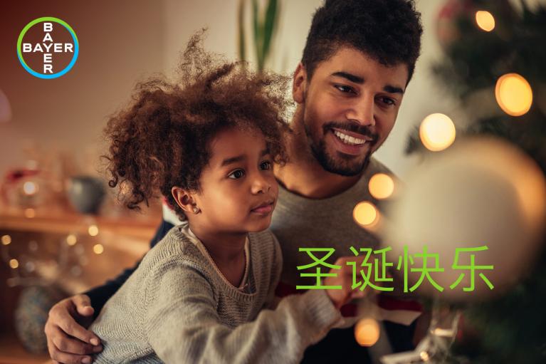 A man and a child decorate a Christmas tree. The words "Merry Christmas" are written in Chinese characters on the image. A Bayer logo is in the top left corner.