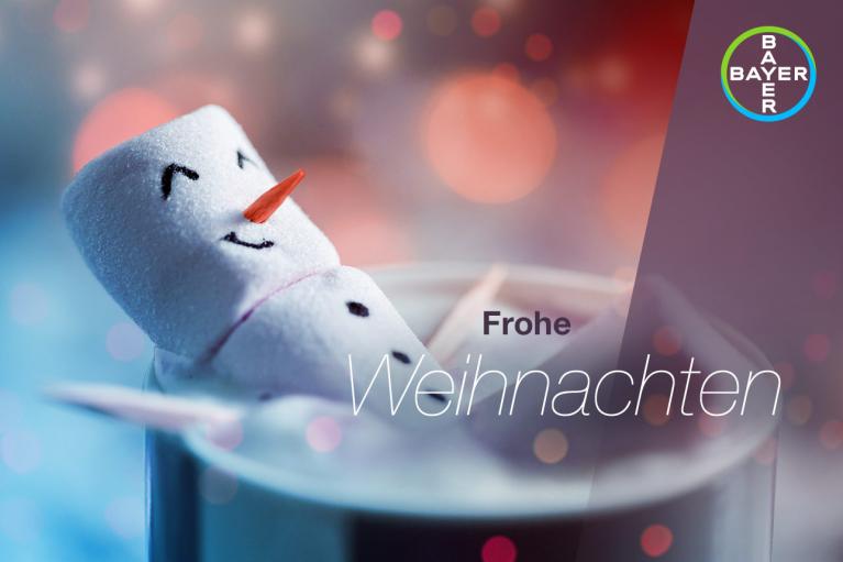 A marshmallow snowman floating in a beverage with "Frohe Weihnachten" text and Bayer logo on the side.