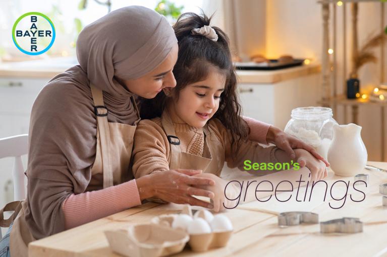 A woman and a child wearing aprons bake together in a kitchen. Text reads "Season's greetings.