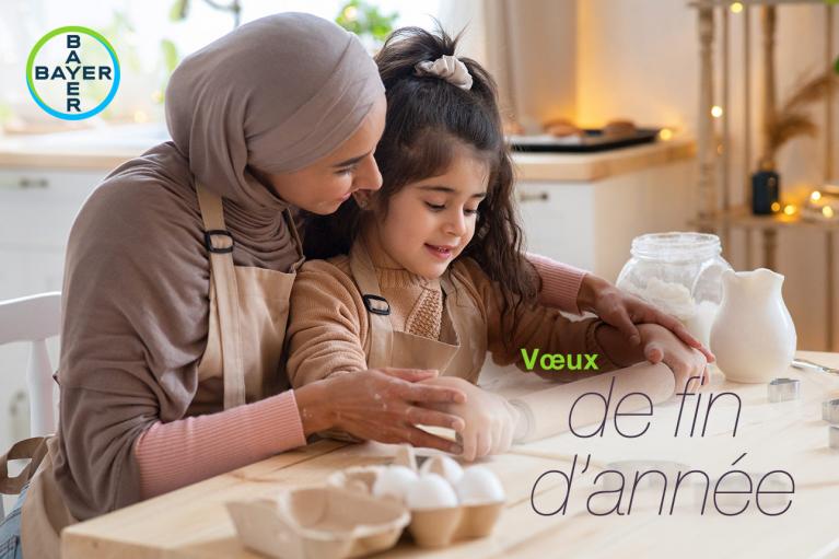 A woman and a child wearing aprons knead dough together in a kitchen. The text "Vœux de fin d'année" and "Bayer" logo are overlaid on the image.