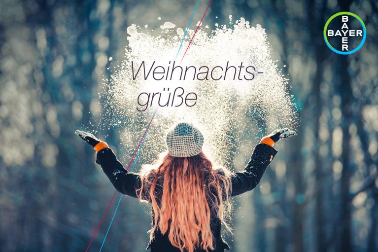 Person in winter clothing throws snow in the air with "Weihnachtsgrüße" text, Bayer logo in corner.