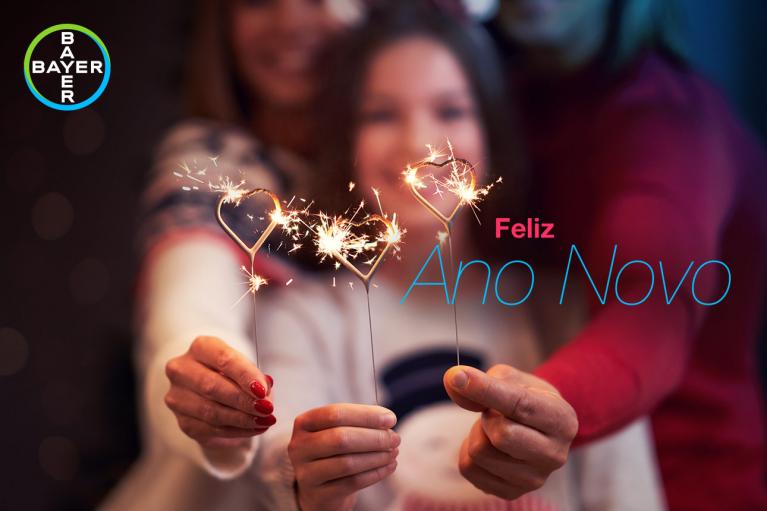 Three people holding sparklers with a blurred background. Text reads "Feliz Ano Novo" and features a Bayer logo.
