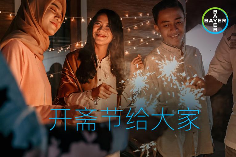 Three people smiling and holding sparklers. Text appears in Chinese characters. Bayer logo in the corner.