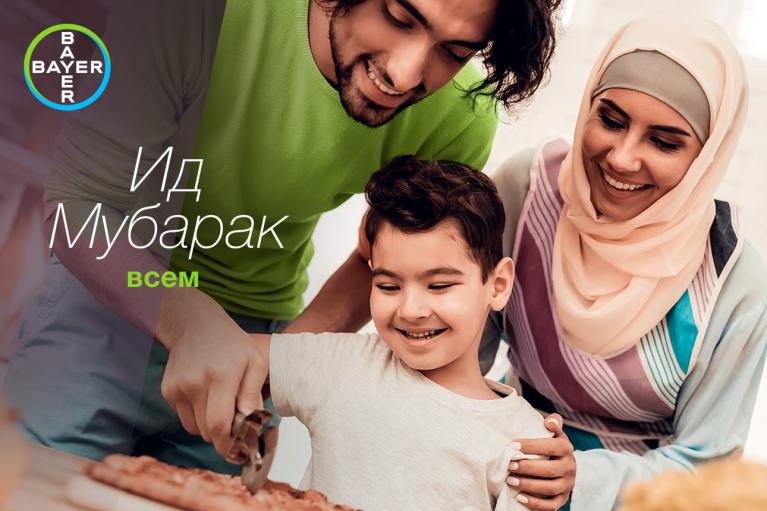 A family smiles while cutting a dessert. The text on the image reads "Ид Мубарак всем" and features the Bayer logo.