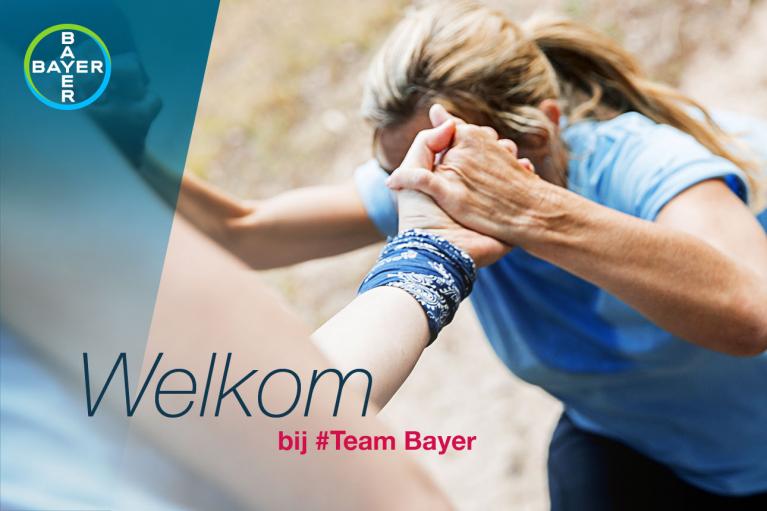 Two people in athletic attire giving a supportive hand clasp outdoors. The image has a Bayer logo and text: "Welkom bij #Team Bayer" on the left.