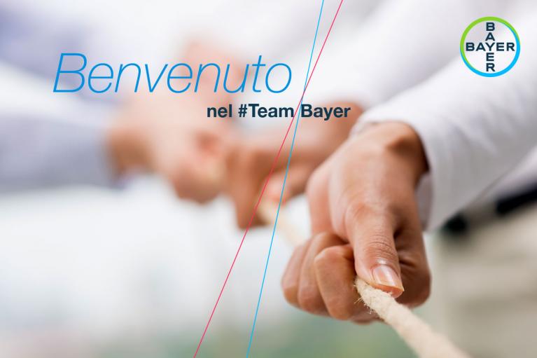 Close-up of two people participating in a tug-of-war game. Text reads "Benvenuto nel #TeamBayer" with Bayer logo in the top right corner.