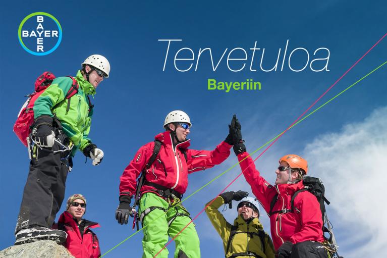 Five climbers in colorful gear celebrate on a snowy mountain peak. Finnish text "Tervetuloa Bayeriin" and Bayer logo are visible.