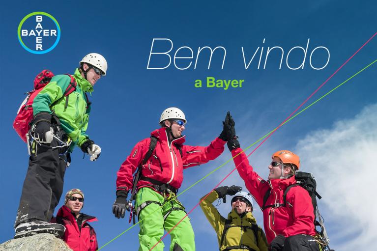 Group of climbers in winter gear high-five on a snowy peak, with a "Bem-vindo a Bayer" message above them.
