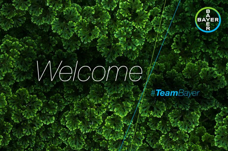 Aerial view of green foliage with the word "Welcome" and hashtag "#TeamBayer" overlaid. Bayer logo in the top right corner.