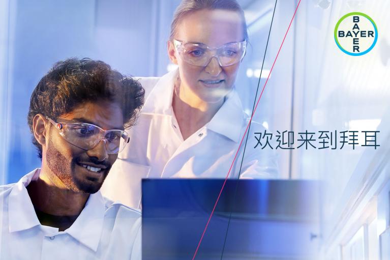 Two scientists in a lab wearing safety goggles and lab coats look at a screen. Bayer logo in the corner. Chinese text on the right.