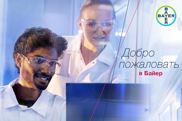 Two scientists wearing lab coats and safety goggles work together in a lab. The Bayer logo is in the top right corner, with Russian text meaning "Welcome to Bayer.
