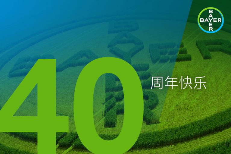 Green and blue image with the number 40, Chinese characters for "Happy Anniversary," and the Bayer logo in the top right corner. A crop field shows the Bayer logo cut into it.