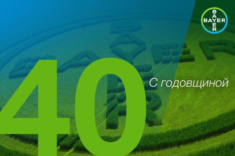 Aerial view of a field with Bayer logo carved into the crops. Large number 40 and Russian text "С годовщиной" overlaid. Bayer logo in the top right corner.