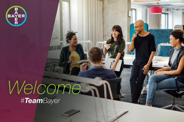 Five people are smiling and talking in an office setting, with a "Welcome #TeamBayer" text overlay and the Bayer logo in the corner.
