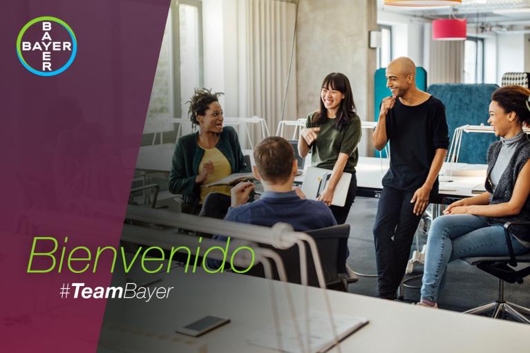 Group of five people standing and sitting in a modern office, engaged in conversation and smiling. "Bienvenido #TeamBayer" text overlay on the left.