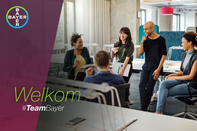 A group of five people sit and stand around a table, smiling and engaging in conversation. The text on the image says "Welkom #TeamBayer" with the Bayer logo.