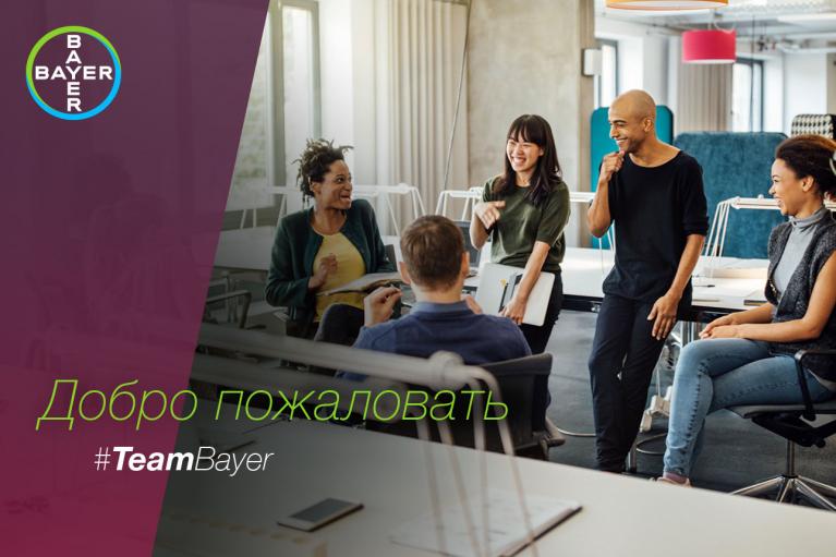 A group of five people are talking and laughing in a modern office setting with the Bayer logo and Russian text saying "Добро пожаловать #TeamBayer" on a purple overlay.