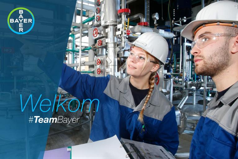 Two workers in safety gear examine equipment in an industrial setting. The Bayer logo is visible, accompanied by text reading "Welkom #TeamBayer.