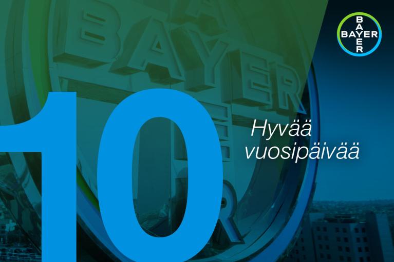 The image features the Bayer logo with a large blue number 10 and the Finnish text "Hyvää vuosipäivää" on a green and blue background.