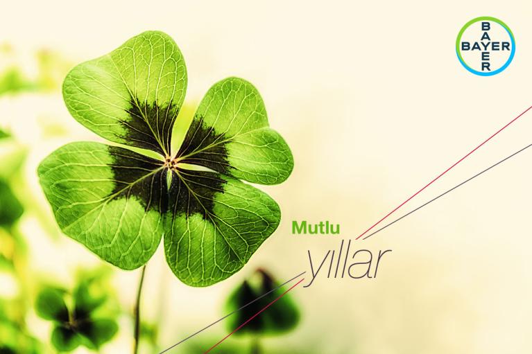A close-up of a four-leaf clover with a central dark patch, accompanied by the text "Mutlu yıllar" and a Bayer logo in the upper right corner.