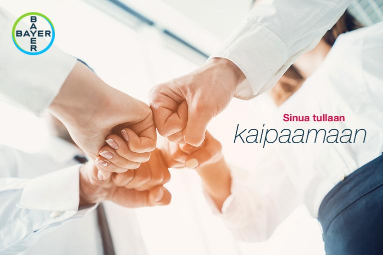 Four people in business attire perform a group fist bump. The Bayer logo is in the top left corner, with Finnish text on the right.