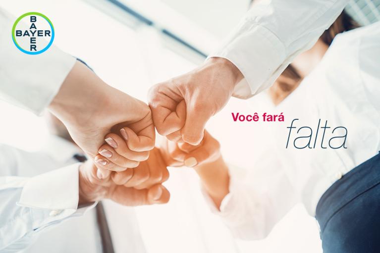 Four people in business attire are doing a fist bump. The text reads "Você fará falta" with the Bayer logo in the top left corner.