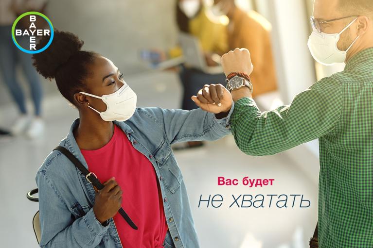Two masked people greet each other with elbow bumps indoors. The Bayer logo is in the top left corner. Russian text is present.