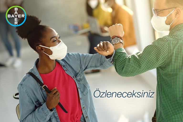 Two people wearing masks greet with an elbow bump indoors. The Bayer logo is in the top left corner. "Özleneceksiniz" is written on the image.