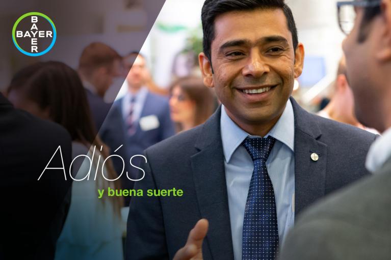 A man in a suit smiles during a conversation at an event. The image features the Bayer logo and the text "Adiós y buena suerte" in Spanish.