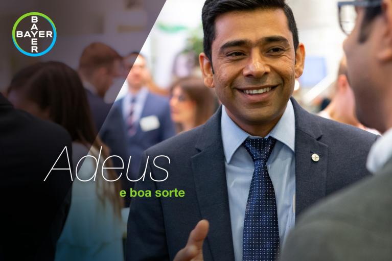 Smiling man in a suit at a social event, with a Bayer logo and Portuguese text "Adeus e boa sorte" on the image.