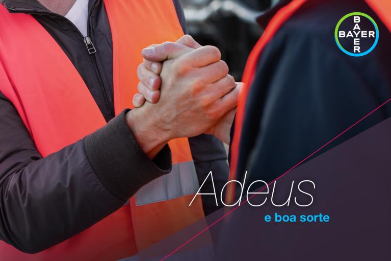 Two people wearing orange vests clasp each other's hands as if in farewell. The text reads "Adeus e boa sorte" with a Bayer logo in the corner.