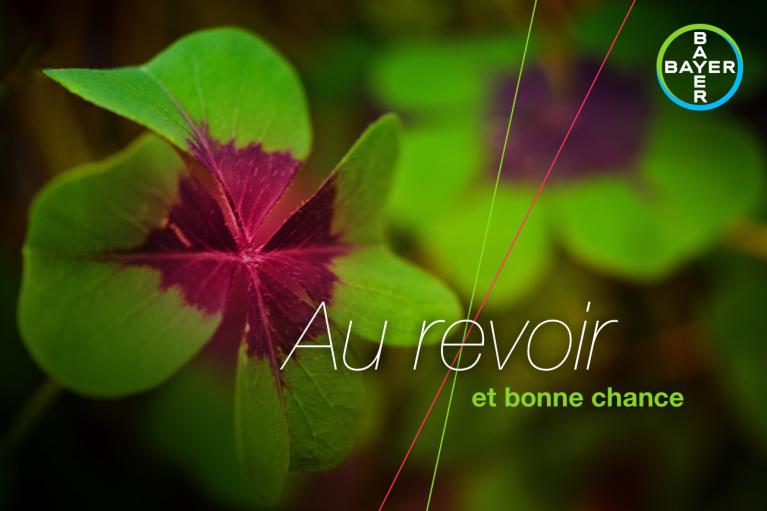 A green and purple four-leaf clover with the text "Au revoir et bonne chance" next to a Bayer logo.