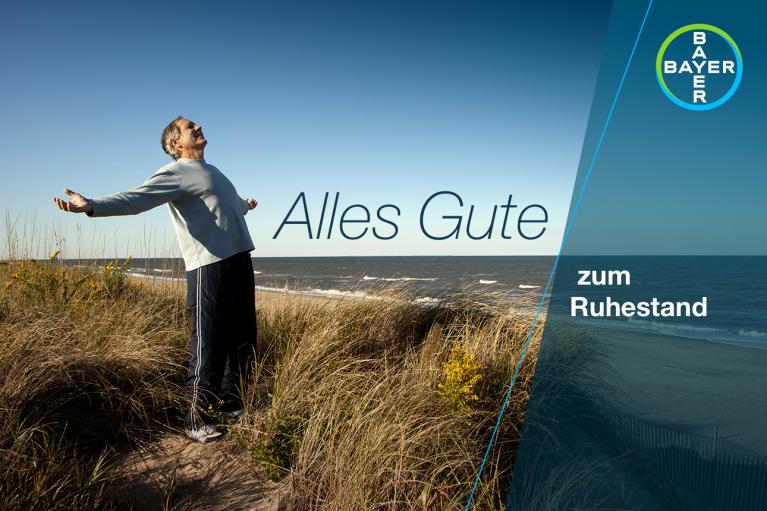 A person stands in a grassy area near the ocean, arms outstretched, with the text "Alles Gute zum Ruhestand" and a Bayer logo.